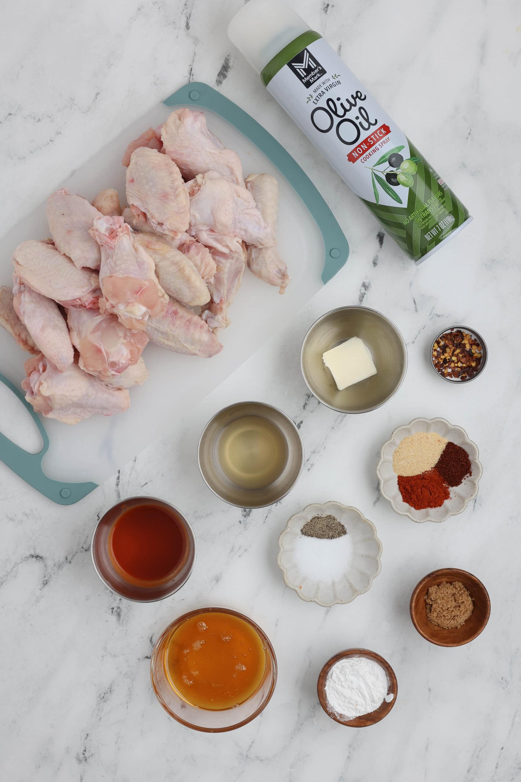 Flat lay of ingredients for hot honey chicken wings including raw chicken wings, honey, hot sauce, spices, butter, apple cider vinegar, and baking powder.