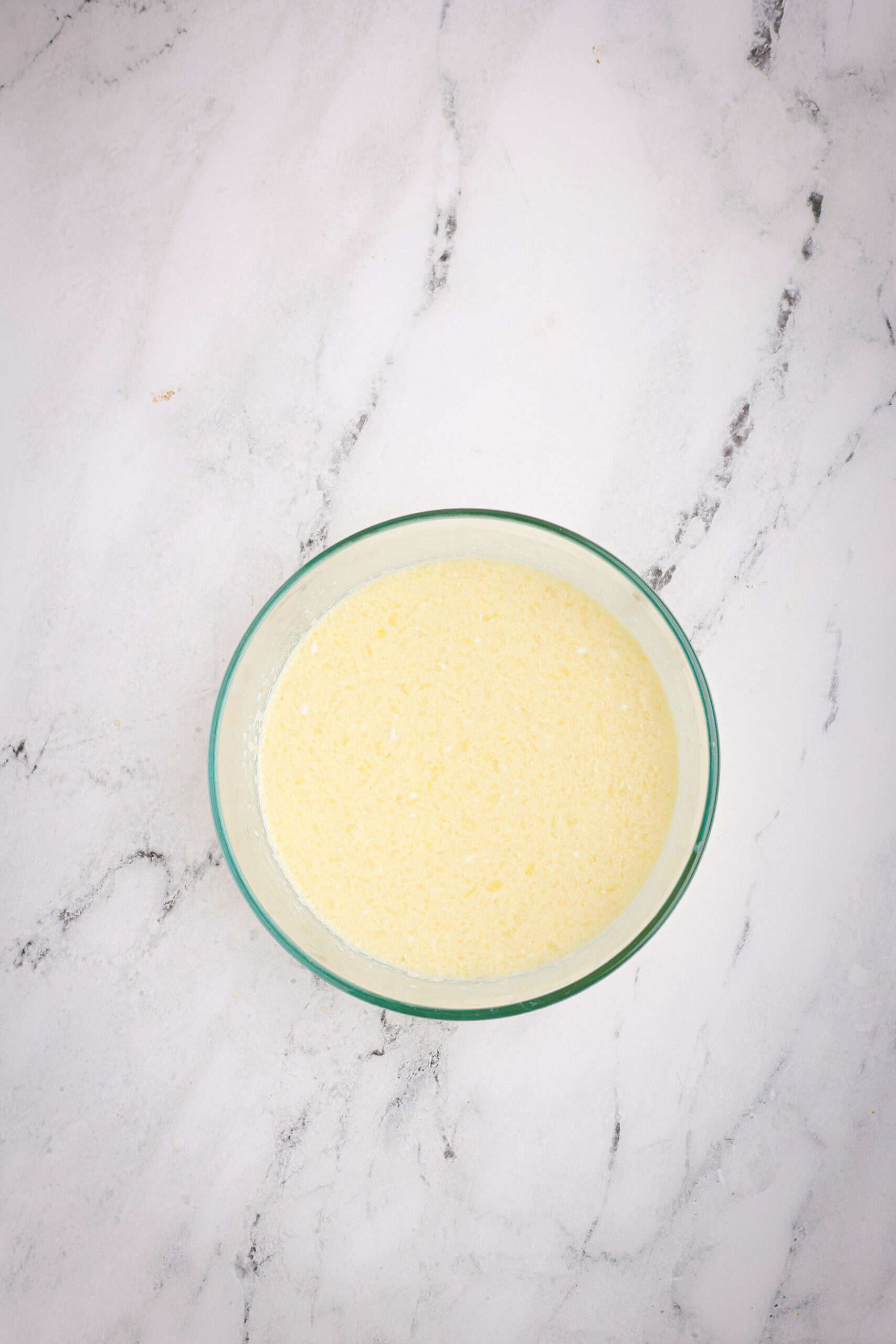 Glass bowl showing the wet ingredients whisked together for the cornbread batter, including buttermilk, eggs, melted butter, and sour cream.