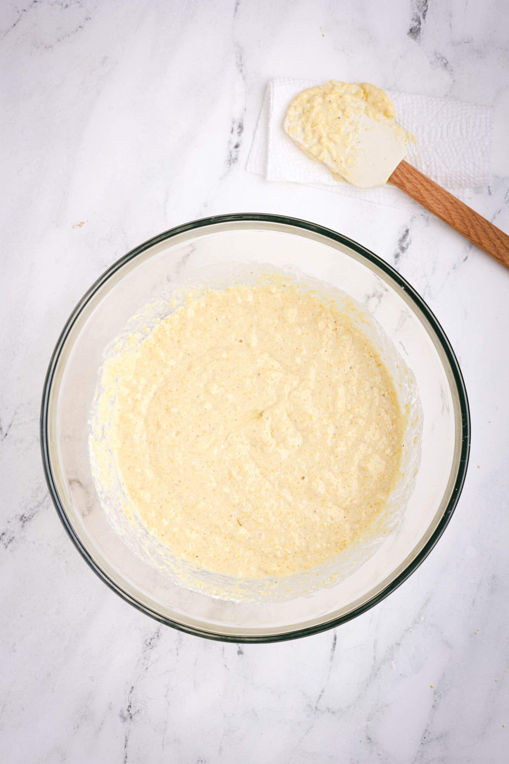 Cornbread batter coming together in a large glass bowl, showing a slightly thick, textured consistency.