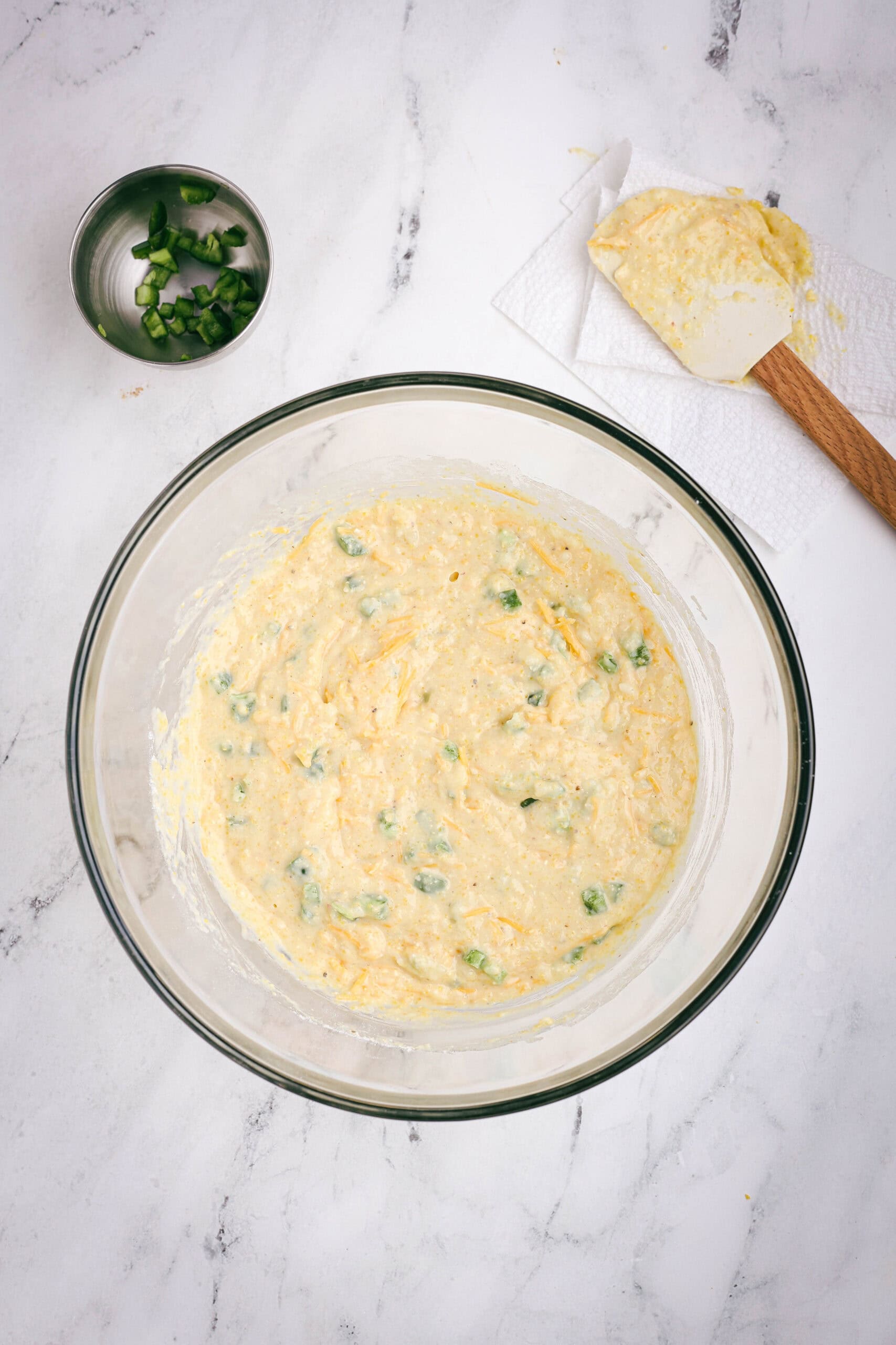 Cornbread batter with chopped jalapeños and shredded cheddar folded in, ready to be spooned into the muffin pan.