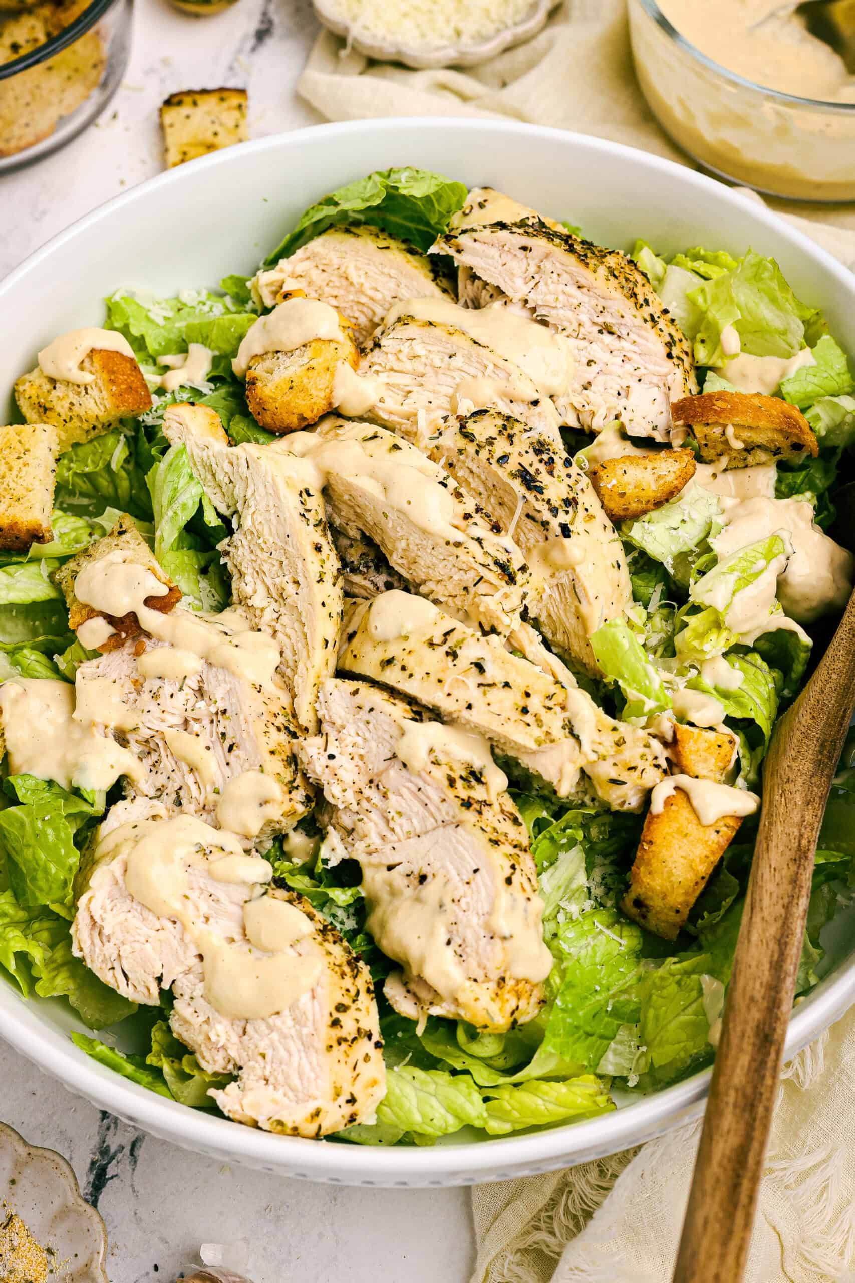 Chicken Caesar salad with sliced seasoned chicken breast, crisp romaine lettuce, homemade croutons, and creamy Caesar dressing in a white bowl