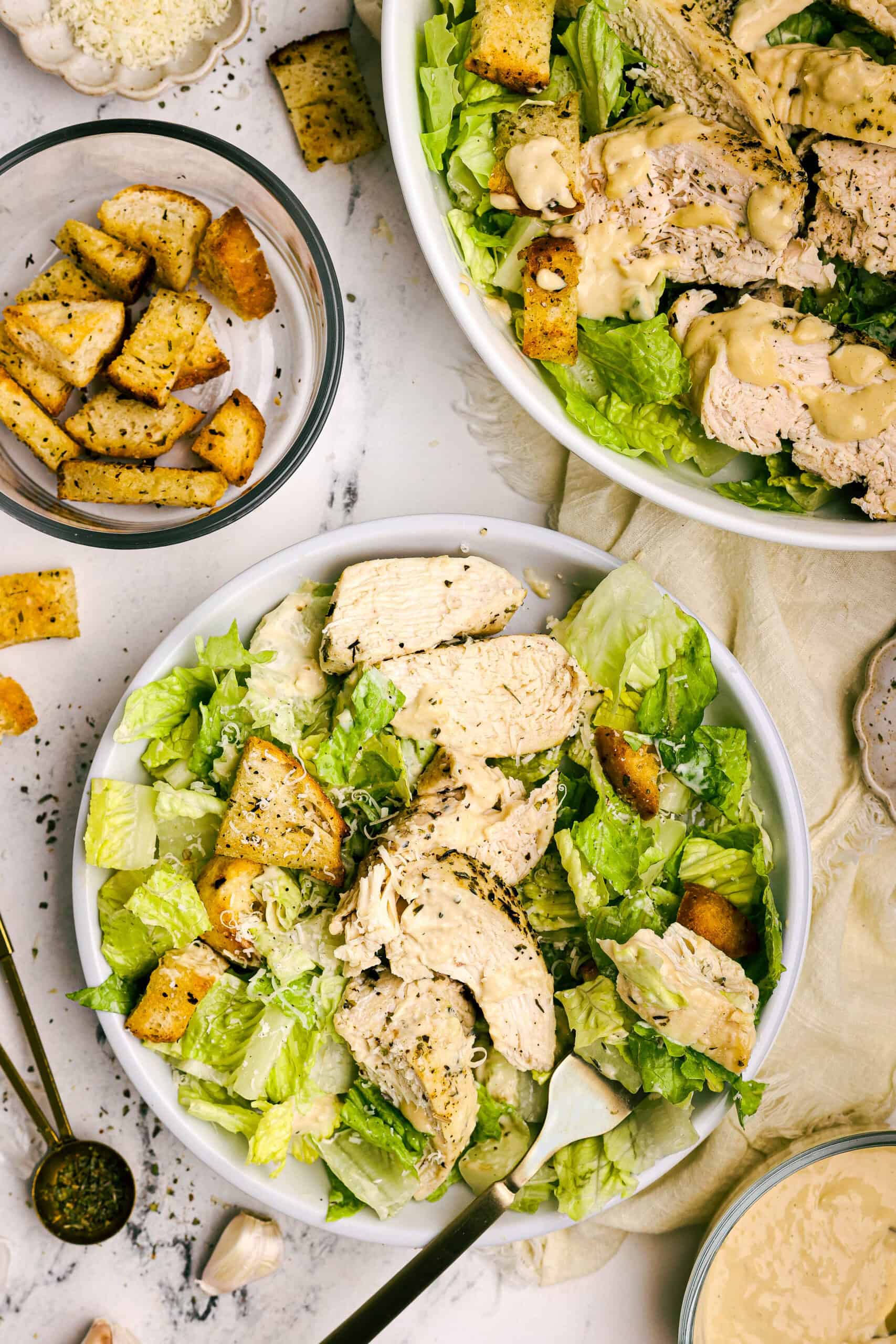 Overhead view of homemade chicken Caesar salad topped with grilled chicken, golden garlic croutons, and shaved Parmesan cheese