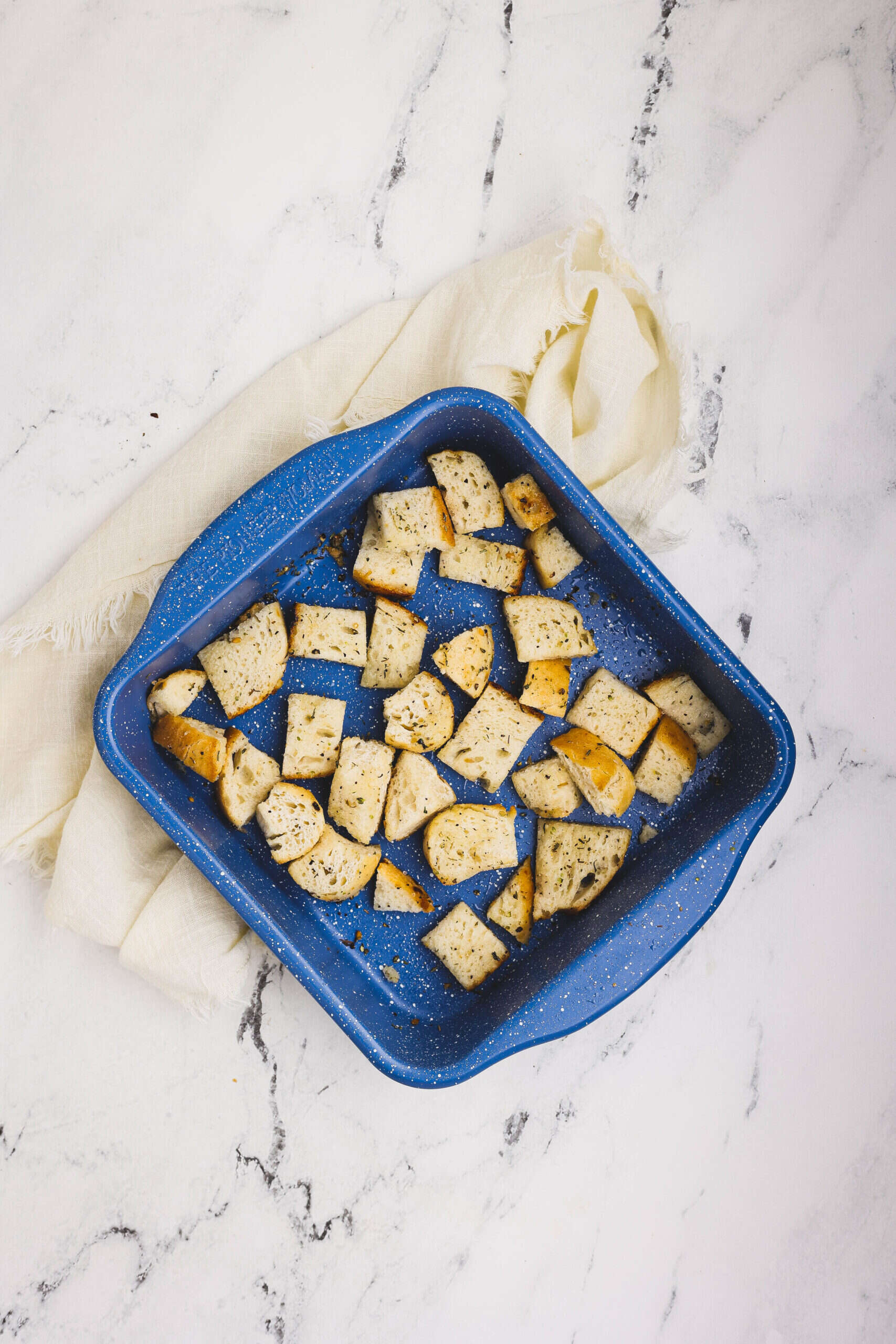 Homemade croutons made from sliced bread seasoned with olive oil and herbs in a baking dish