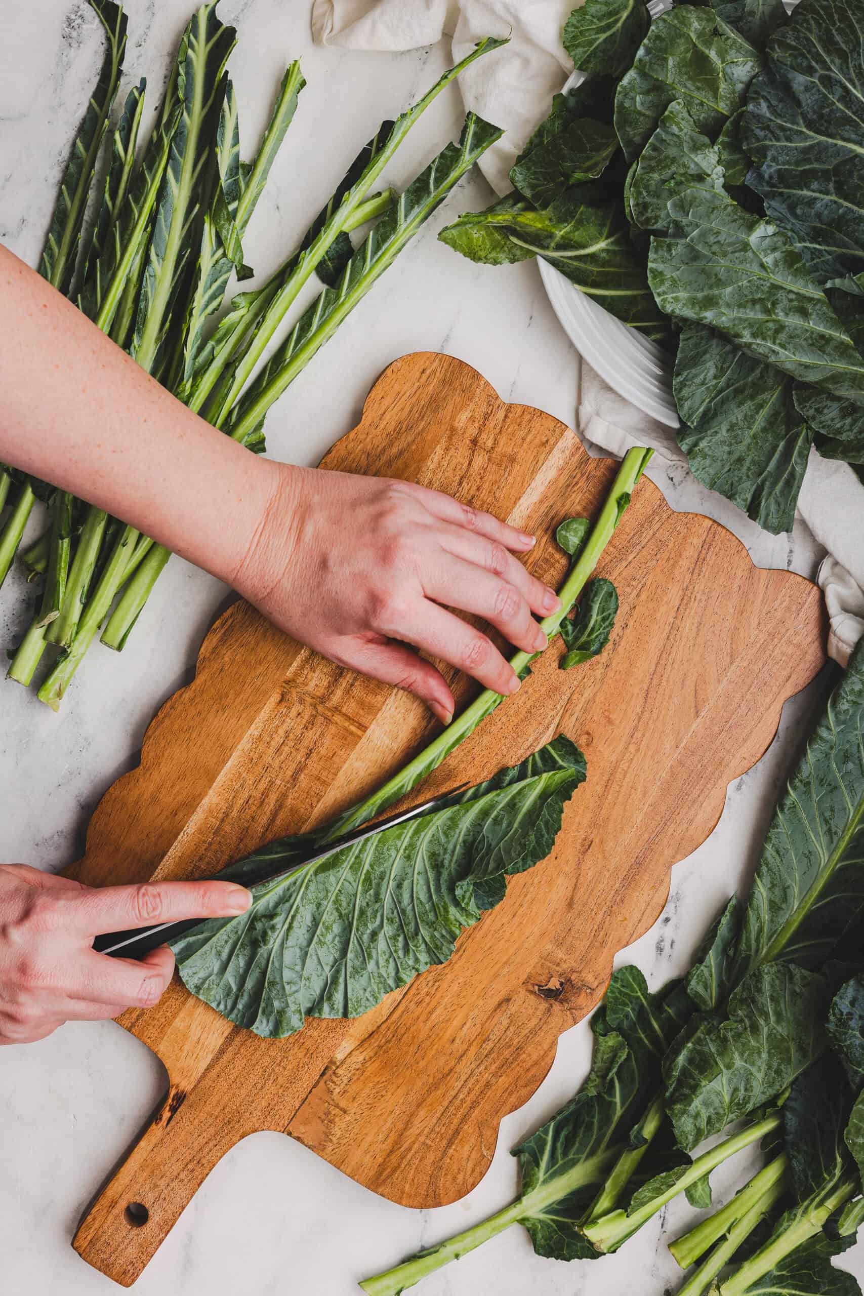 Removing stems from collard green leaves on a wooden cutting board.