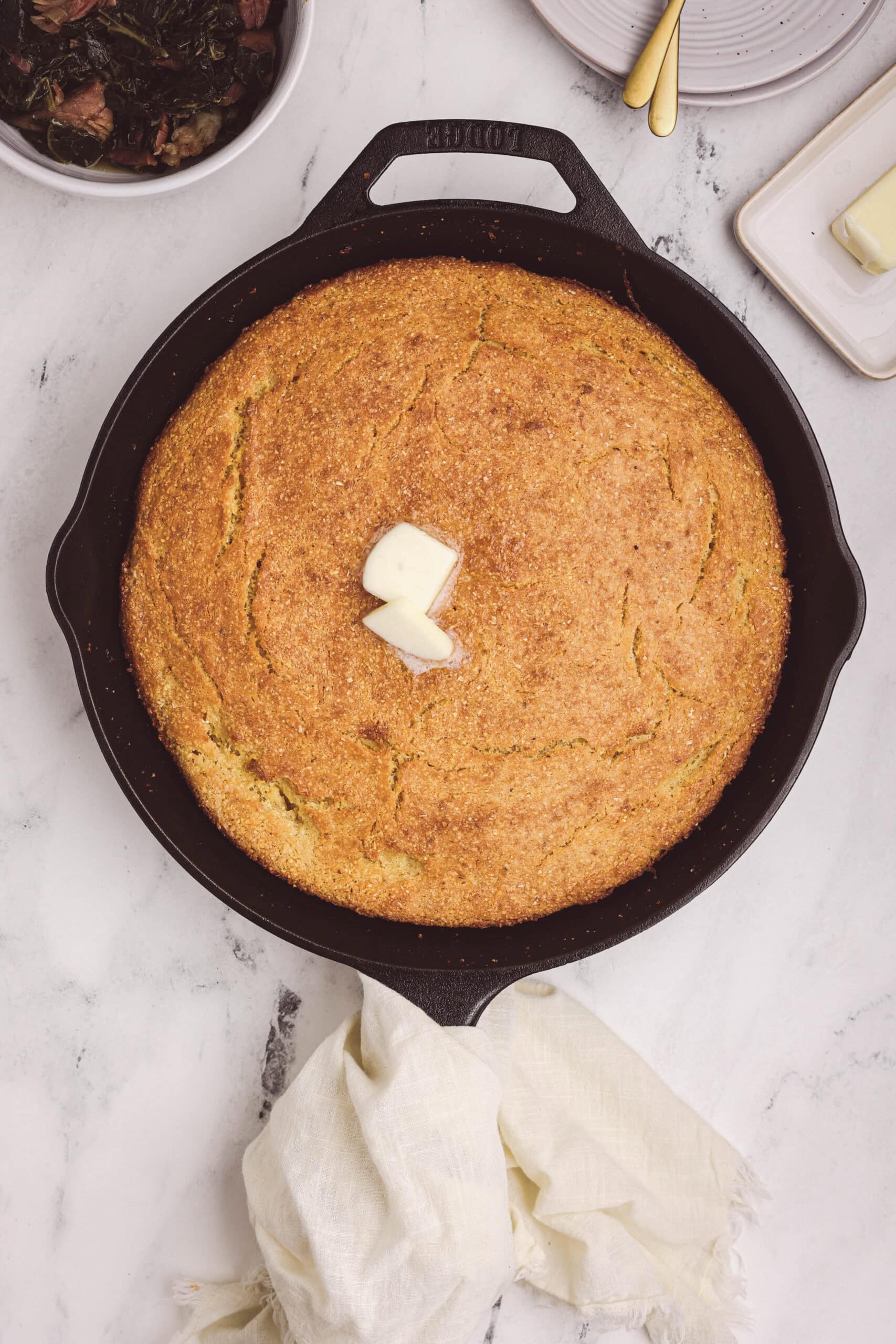 Golden cast iron skillet cornbread with melted butter on top, baked until crisp and golden.
