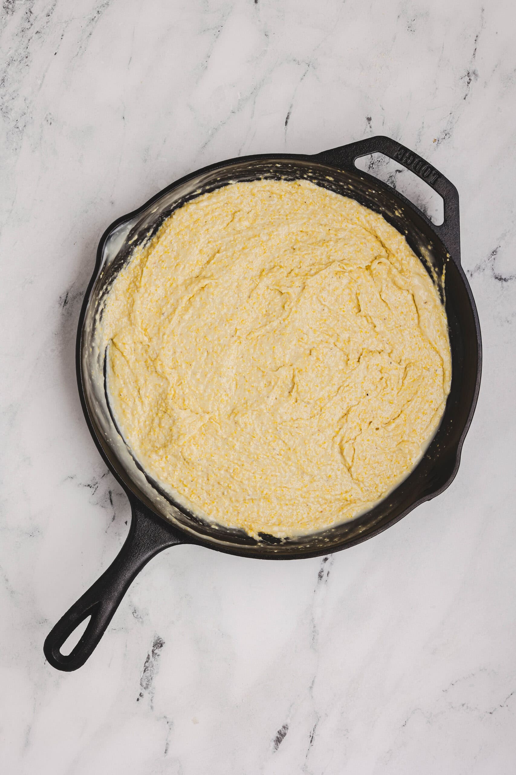 Cornbread batter spread evenly in a buttered cast iron skillet.