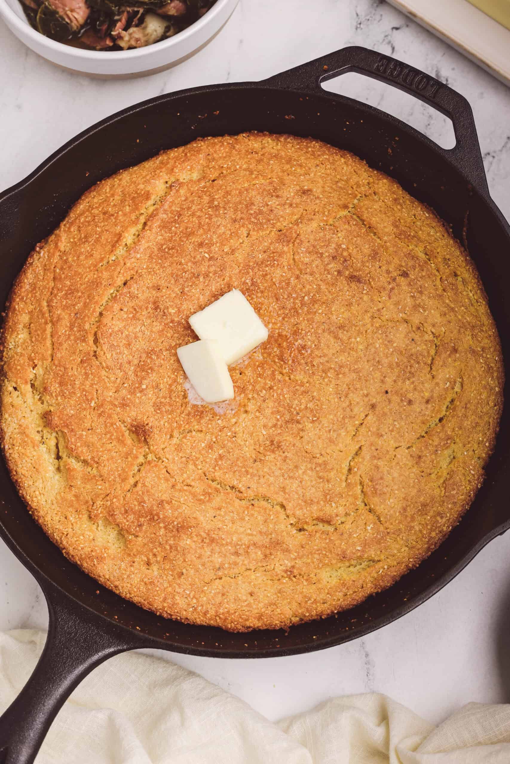 Freshly baked cast iron cornbread with a golden crust and melted butter on top.