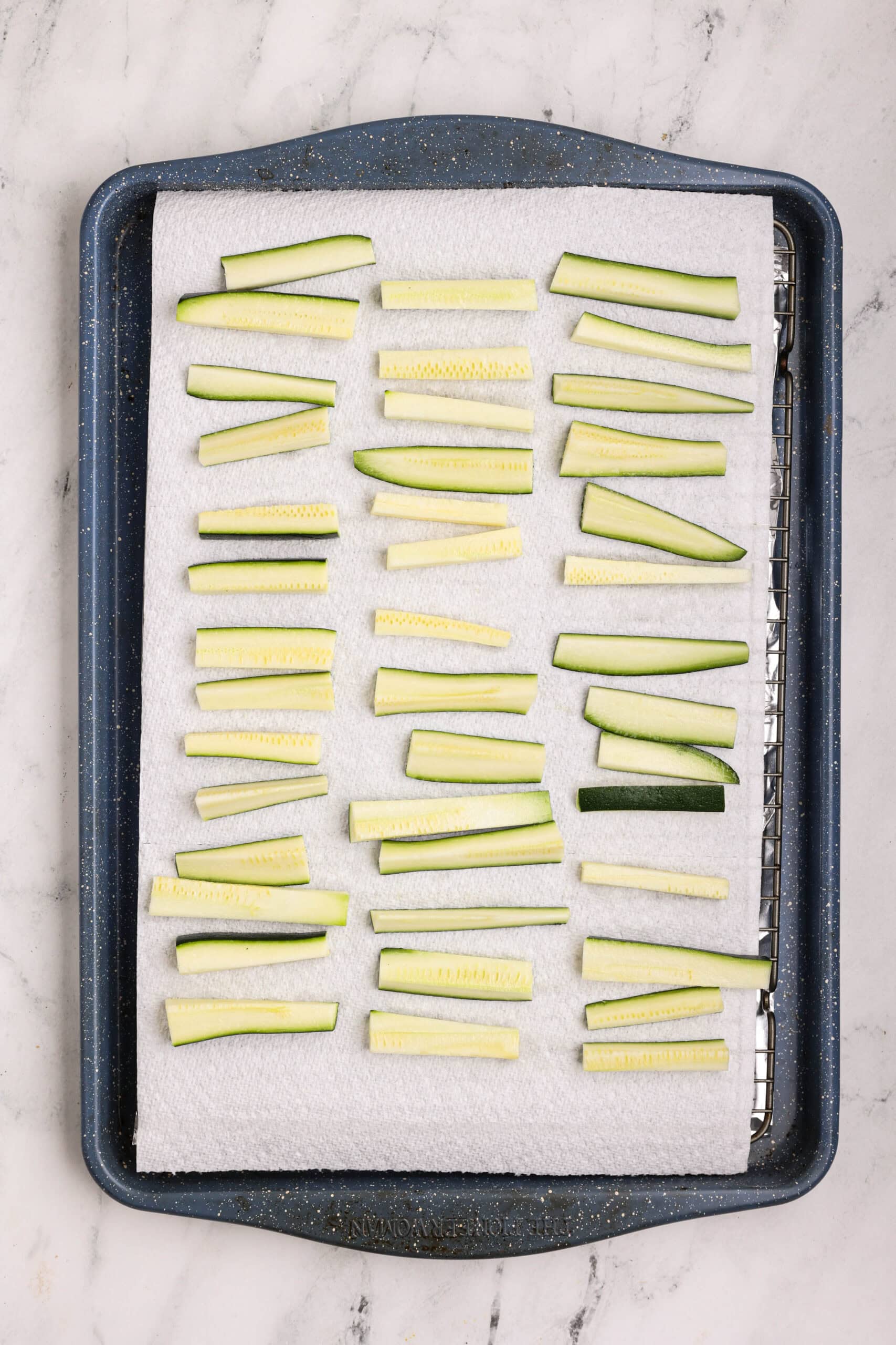 Zucchini sticks spread on paper towels and lightly salted to draw out excess moisture before breading.